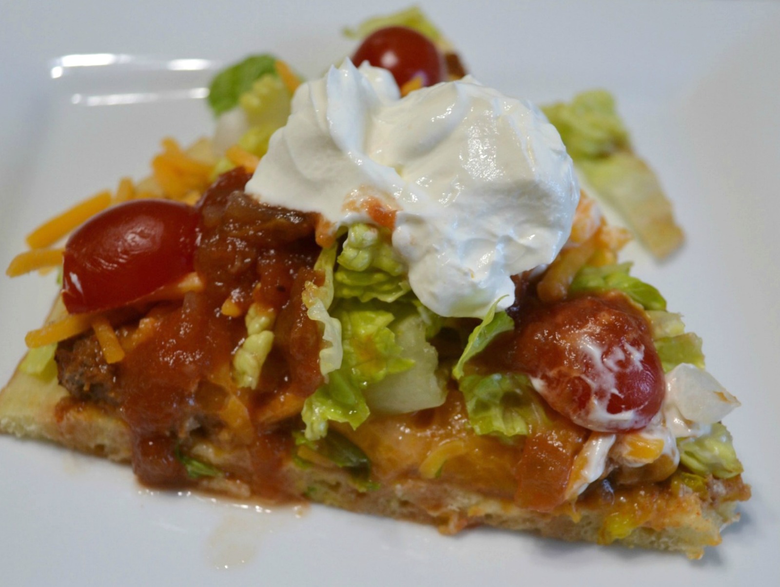 Taco Pizza Supreme is a mexican style pizza loaded with ground beef,sesoings,refried beans and cheese mixture.Taco toppings, sour cream and salsa round it off. 