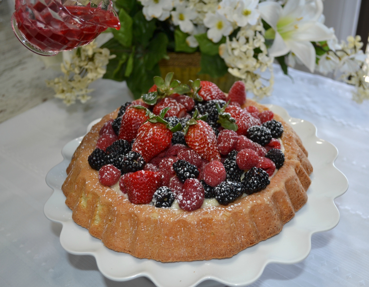 Raspberry Almond Tiara Cake is baked in a tiara pan, has almond paste in the cake, filled with a mascarpone layer and topped with fresh berries. Drizzle fresh raspberry sauce.