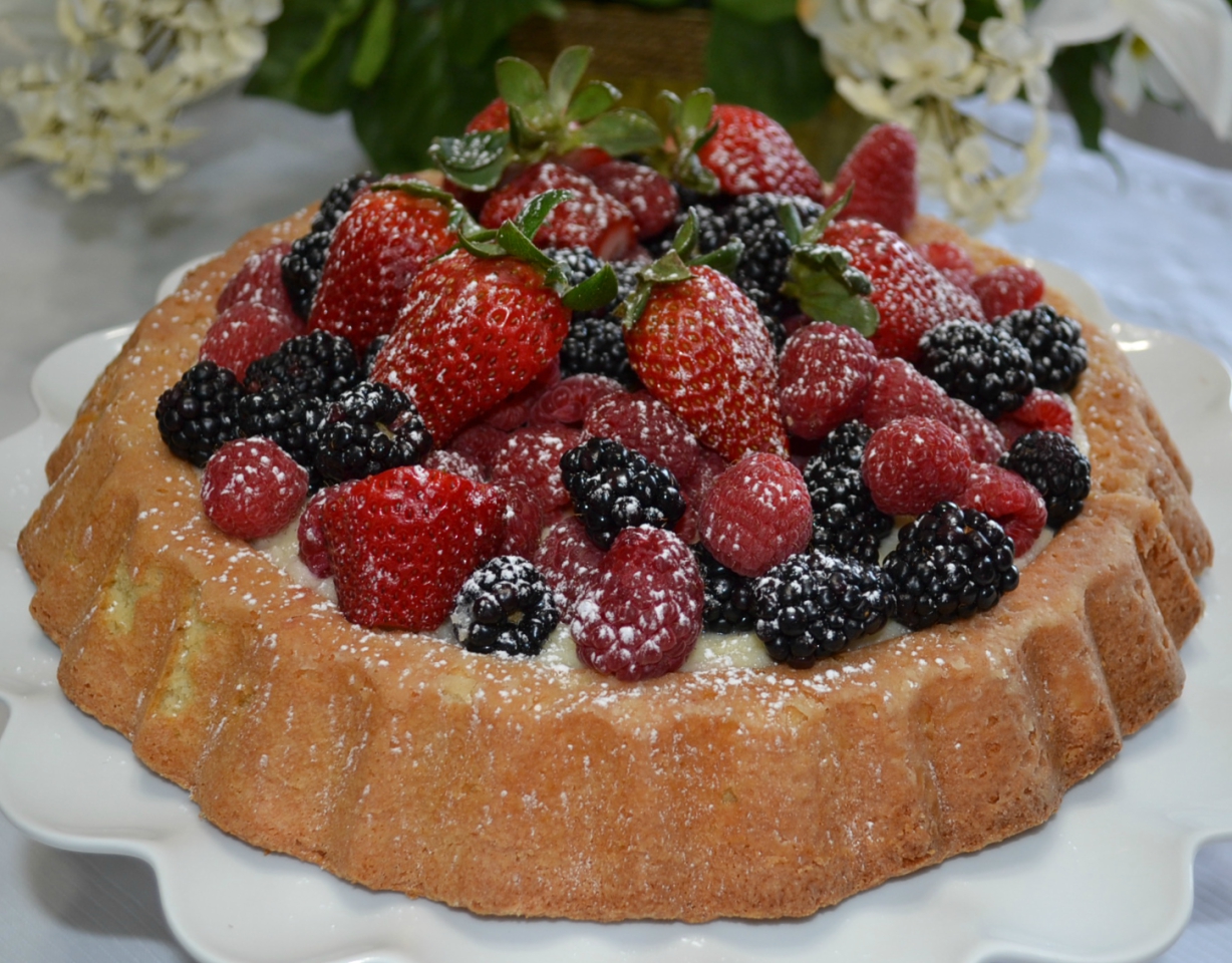 Raspberry Almond Tiara Cake is baked in a tiara pan, has almond paste in the cake, filled with a mascarpone layer and topped with fresh berries. Drizzle fresh raspberry sauce.