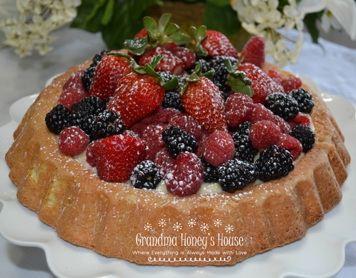 Raspberry Almond Tiara Cake is baked in a tiara pan, has almond paste in the cake, filled with a mascarpone layer and topped with fresh berries. Drizzle fresh raspberry sauce.