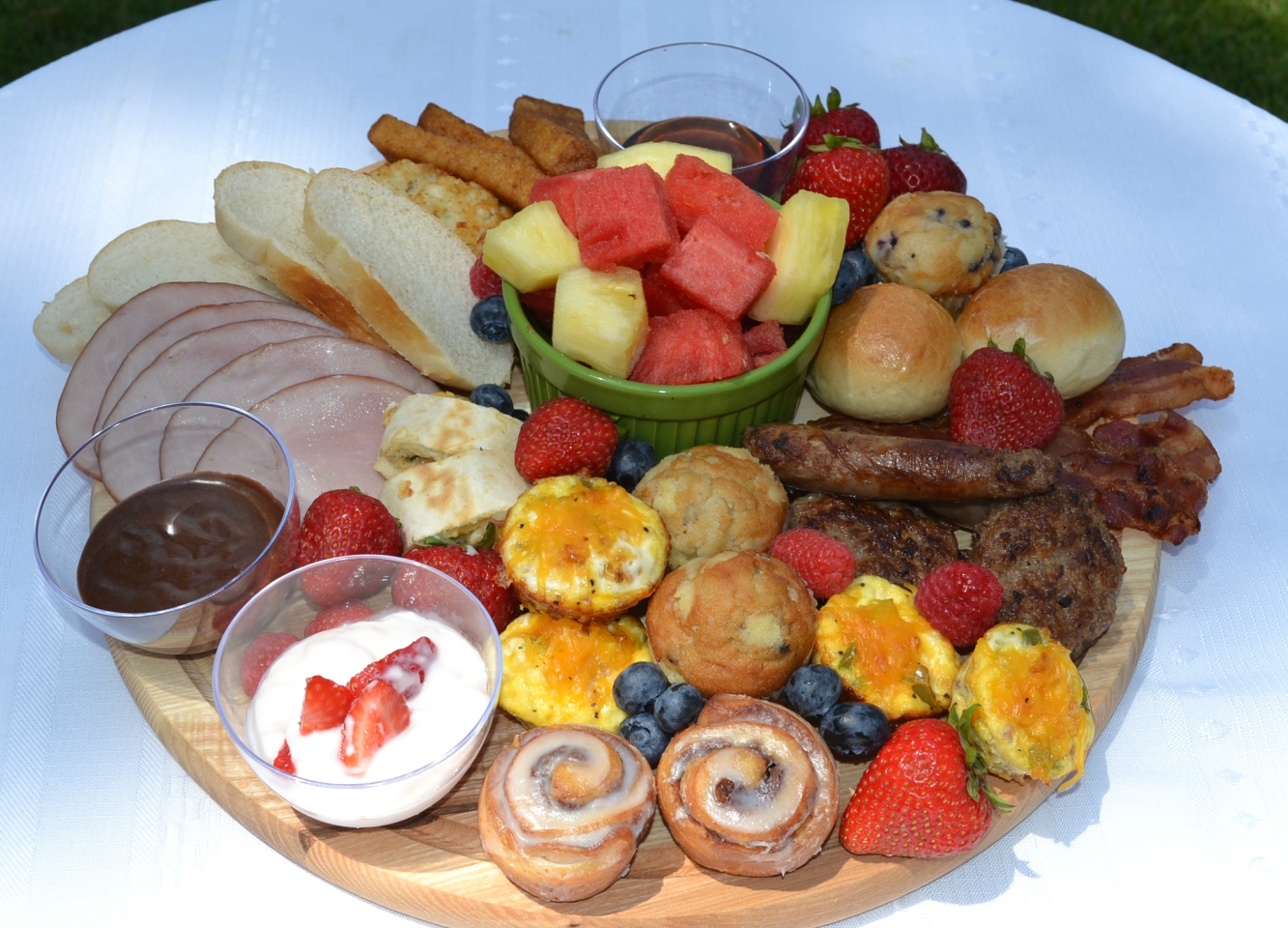 This Brunch Board for 2 is a delicious and fun way to enjoy a start to your day. A round, wooden cutting board is filled with a variety of breakfast foods, fresh fruits, dips, and sweet treats.