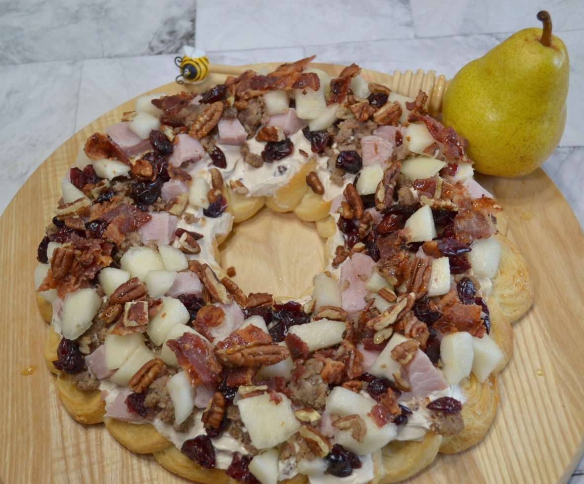 Holiday Pear Appetizer Wreath starts with a crescent crust,honey pecan cream cheese spread and topped with pears,ham,sausage,nuts,bacon,cranberries,and a drizzle of honey.