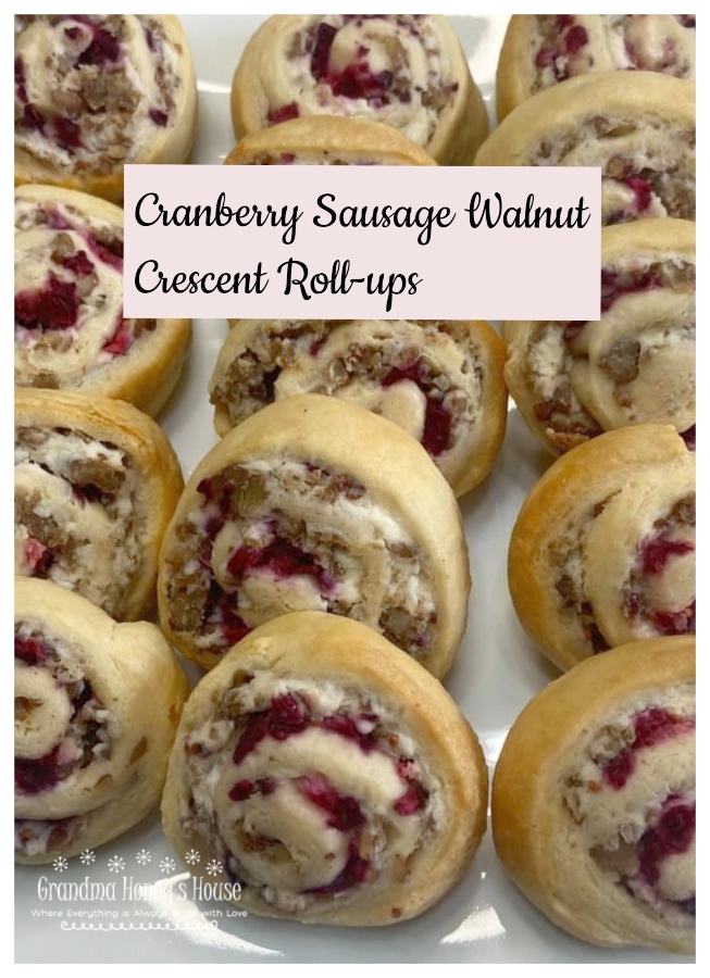 A crescent dough sheet filled with a mixture of cream cheese, cooked sausage crumbles, walnuts, topped with cranberry sauce, then rolled, sliced and baked.