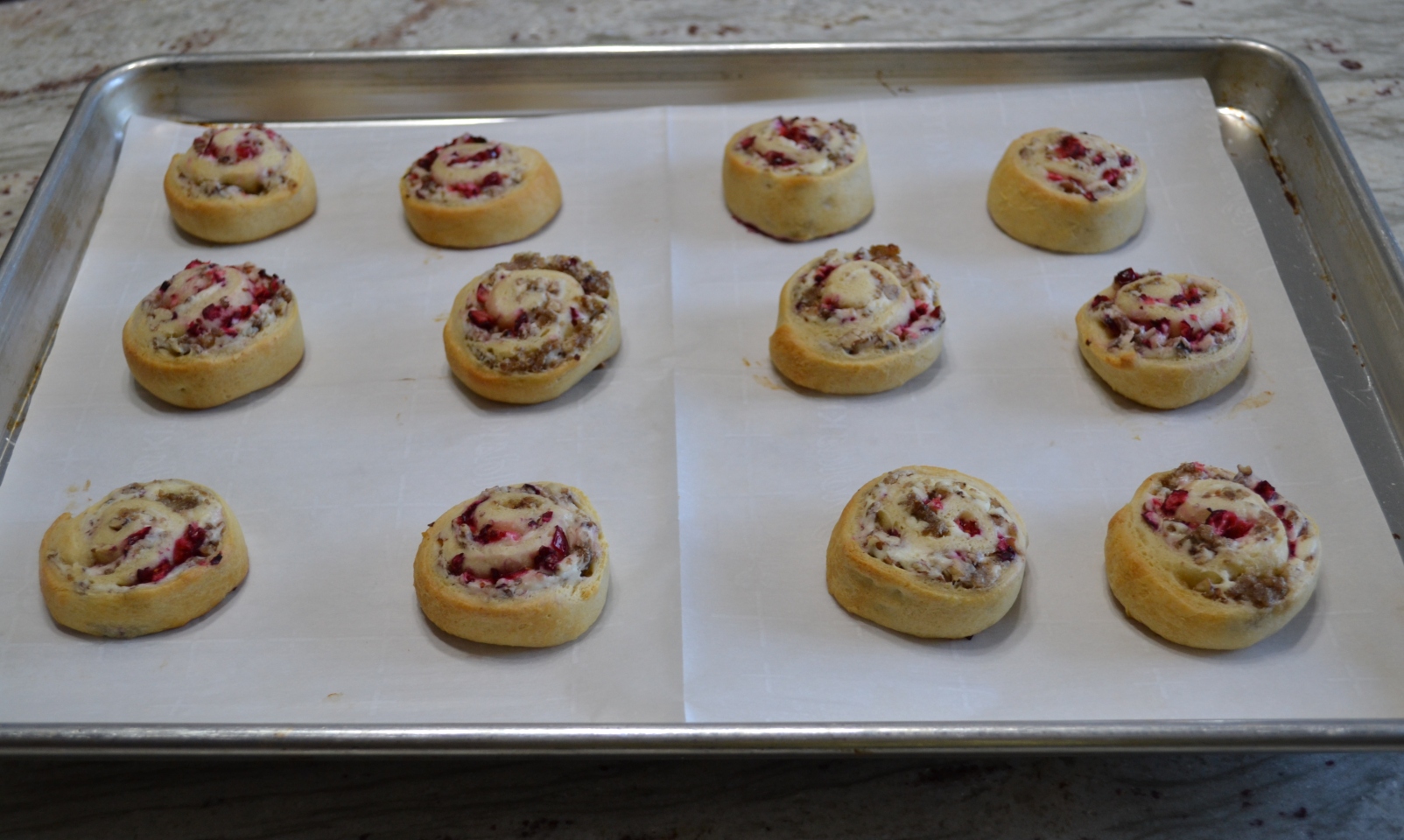 A crescent dough sheet filled with a mixture of cream cheese, cooked sausage crumbles, walnuts, topped with cranberry sauce, then rolled, sliced and baked.