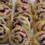 A crescent dough sheet filled with a mixture of cream cheese, cooked sausage crumbles, walnuts, topped with cranberry sauce, then rolled, sliced and baked.