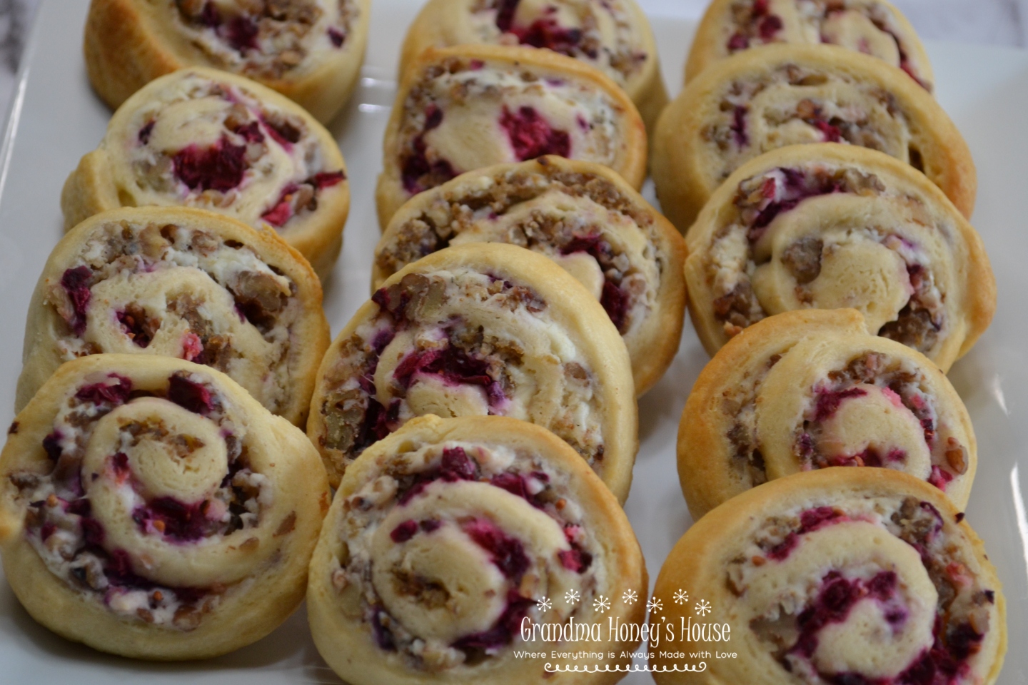 A crescent dough sheet filled with a mixture of cream cheese, cooked sausage crumbles, walnuts, topped with cranberry sauce, then rolled, sliced and baked.