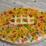 Loaded football veggie pizza is a crescent crust in a football shape, covered with cream cheese filling, veggies, meat and cheese. The perfect appetizer.