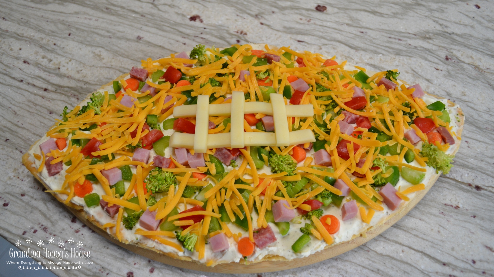 Loaded football veggie pizza is a crescent crust in a football shape, covered with cream cheese filling, veggies, meat and cheese. The perfect appetizer.