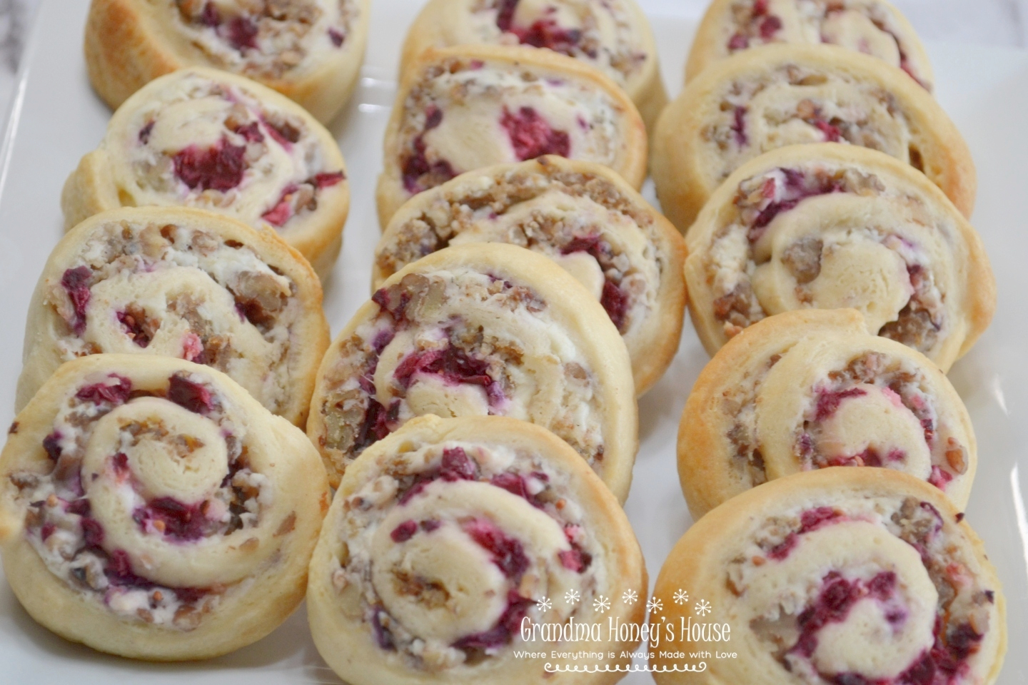 A crescent dough sheet filled with a mixture of cream cheese, cooked sausage crumbles, walnuts, topped with cranberry sauce, then rolled, sliced and baked.
