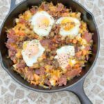 Hearty Grilled Breakfast Skillet, a skillet full of meats, potatoes, veggies, eggs and cheese cooked on the grill in a cast iron skillet.