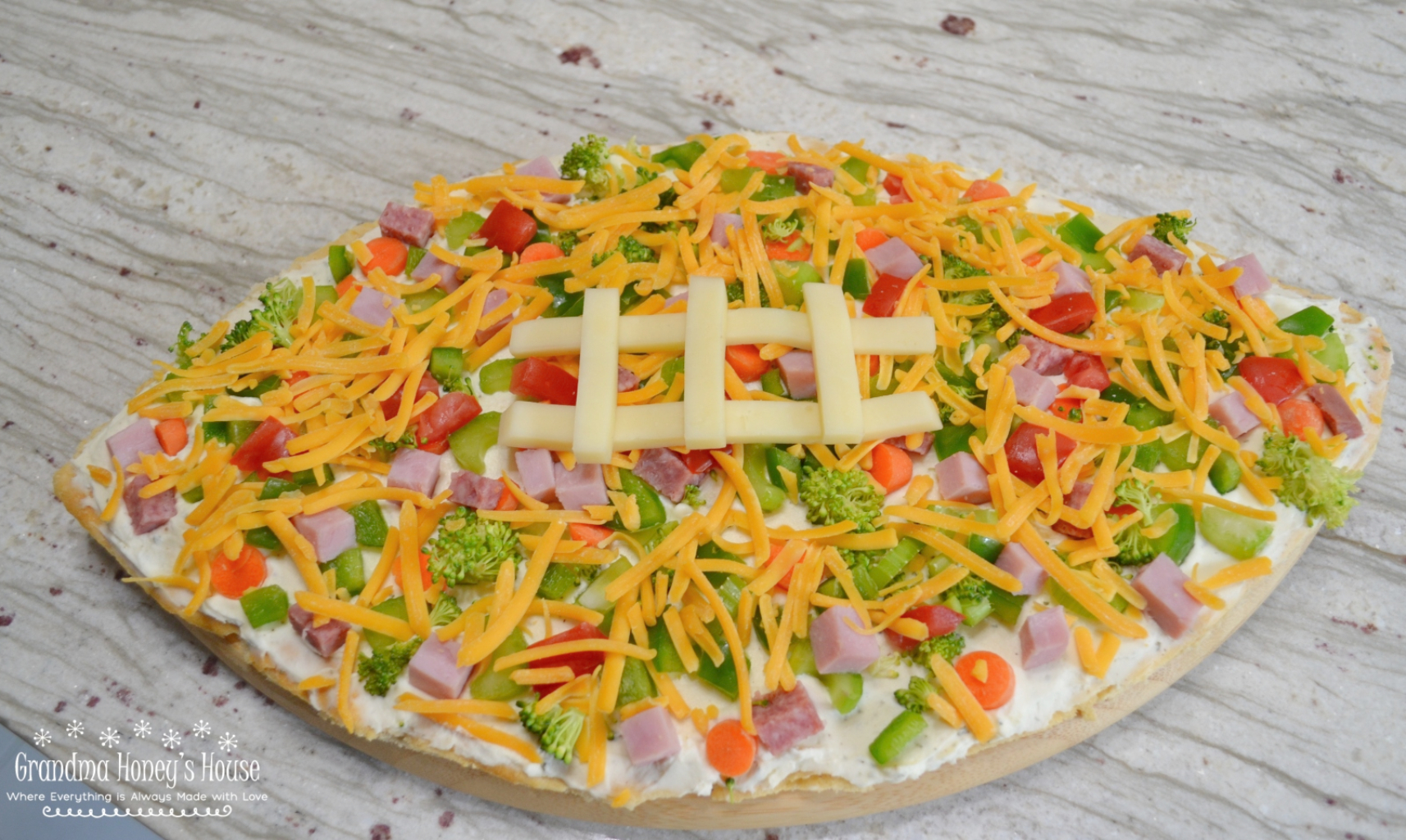 Loaded football veggie pizza is a crescent crust in a football shape, covered with cream cheese filling, veggies, meat and cheese. The perfect appetizer.