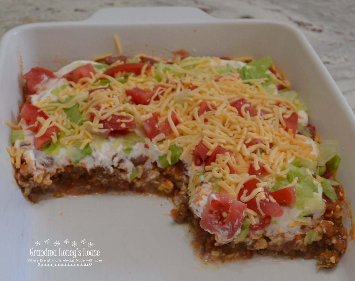 Taco Dip with Meat , a crowd pleasing dip consists of layers of refried beans, seasoned beef, Rotel, cheese, salsa, sour cream, and topped with shredded lettuce, tomatoes, and cheese.&nbsp; Serve with Scoops, Tostitos, or tortilla chips.