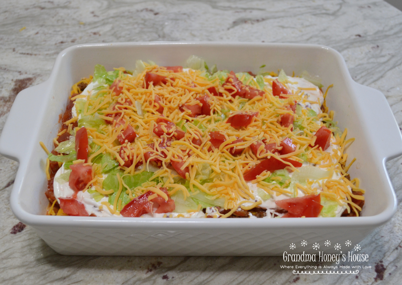 This crowd pleasing dip consists of layers of refried beans, seasoned beef, Rotel, cheese, salsa, sour cream, and topped with shredded lettuce, tomatoes, and cheese.&nbsp; Serve with Scoops, Tostitos, or tortilla chips.